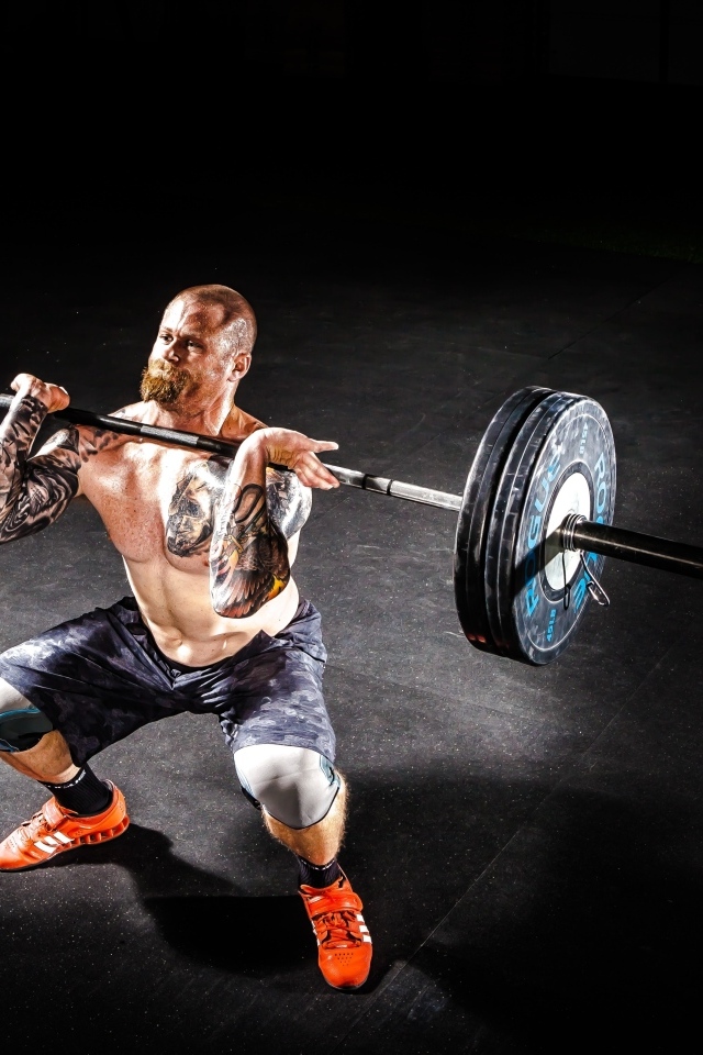 Сильный мужчина с татуировками на теле поднимает штангу