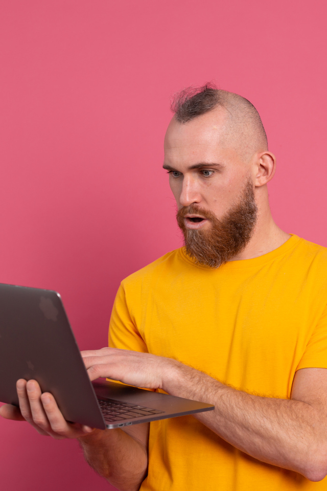 Удивленный мужчина с ноутбуком на розовом фоне