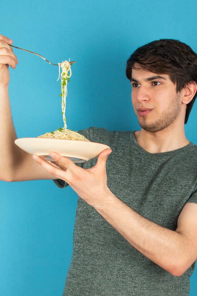 Молодой человек держит тарелку со спагетти в руках