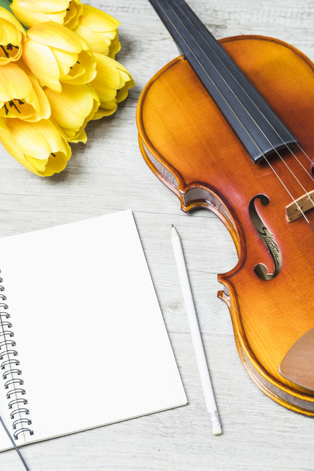 Красивая скрипка на столе с блокнотом, наушниками и букетом тюльпанов
