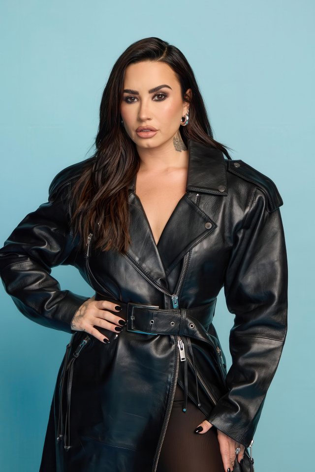 Певица Деми Ловато в кожаном черном пальто на голубом фоне