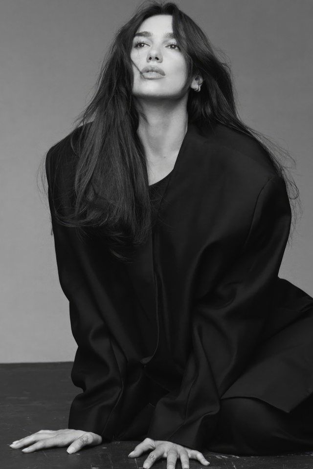 Певица Дуа Липа в черном костюме сидит на полу