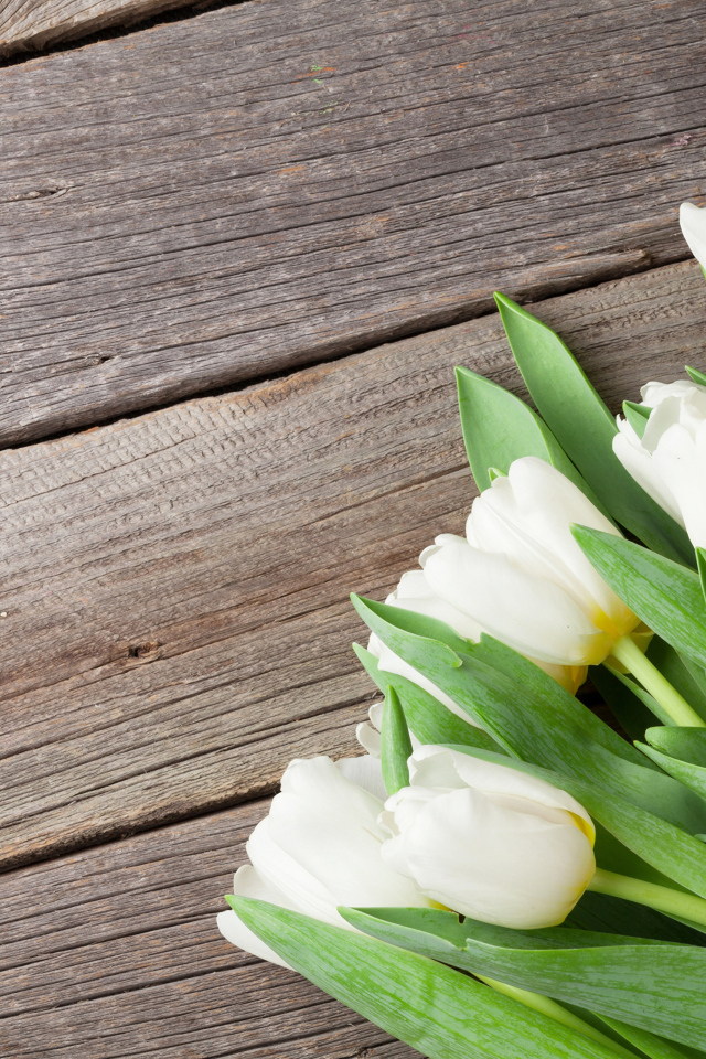 Букет нежных белых тюльпанов с зелеными листьями на деревянном столе