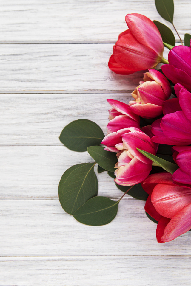 Букет розовых тюльпанов с подарком и зелеными листьями на белом столе