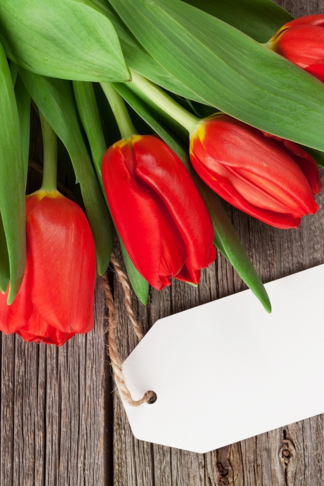 Букет красных тюльпанов с открыткой на деревянном столе
