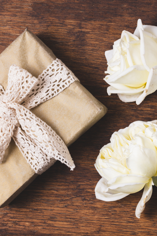 Коробка с подарком на деревянном столе с белыми розами