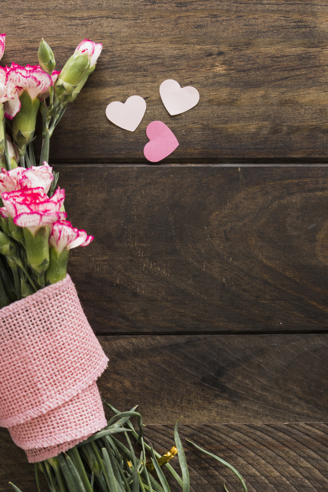 Розовые гвоздики с сердечками на коричневом деревянном фоне