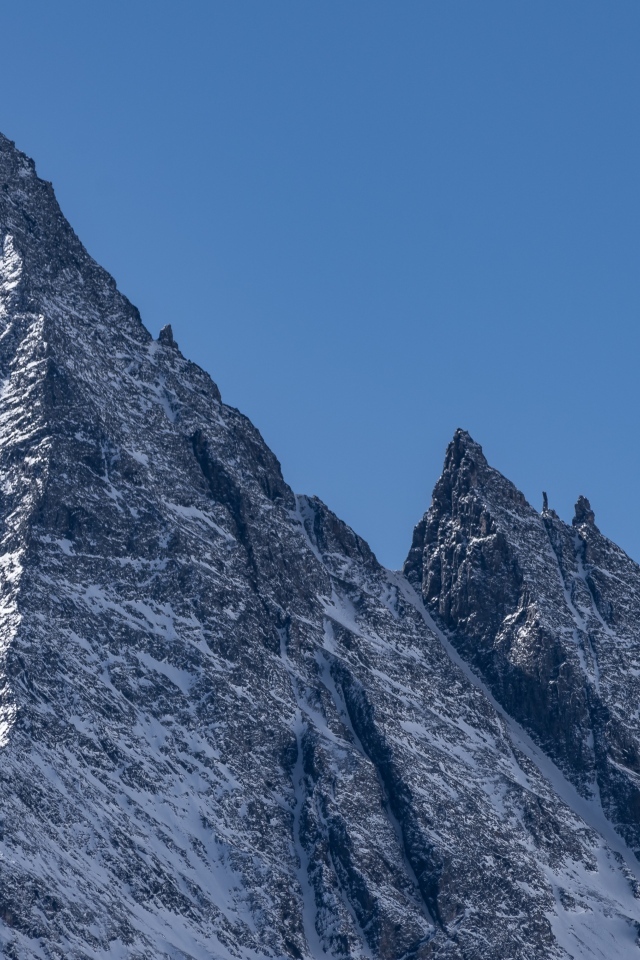 Крутая вершина горы в снегу на фоне голубого неба