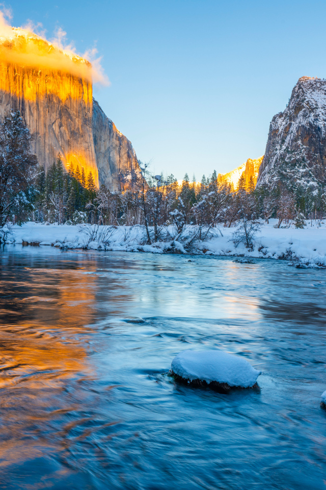 Холодная река с заснеженными берегами и горы в лучах солнца