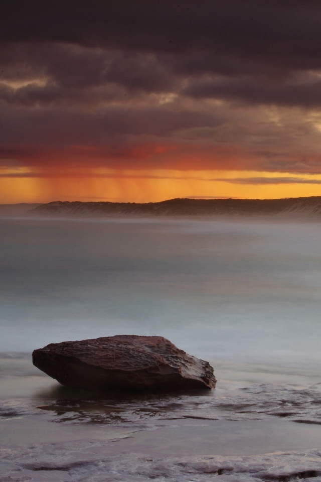 Большой камень в воде на фоне грозового неба в море