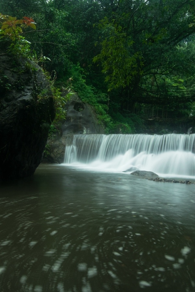 Водопад стекает в реку с большими камнями в лесу