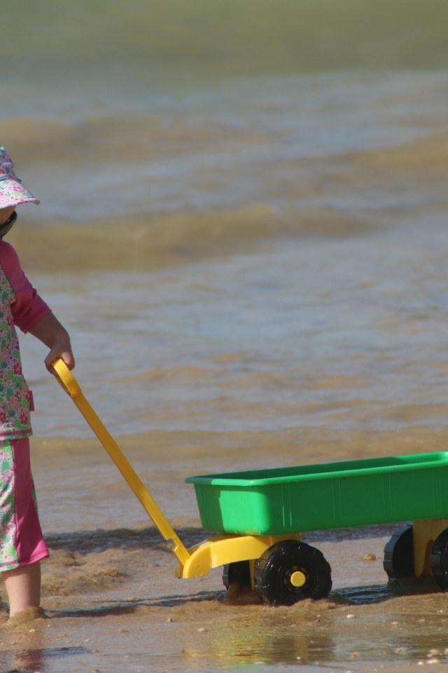 Девочка с машинкой играет на песке у моря