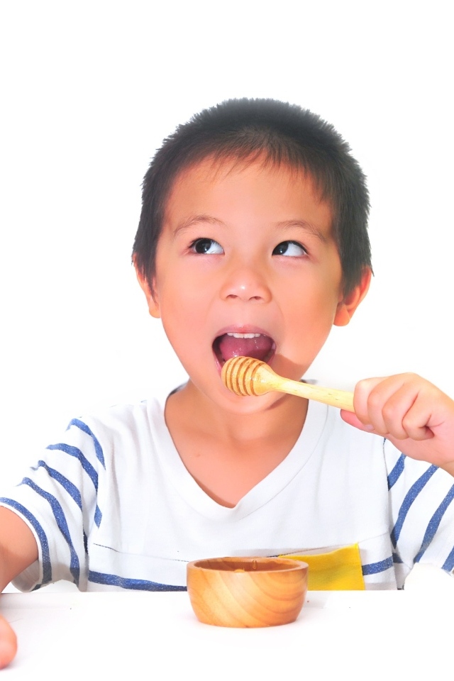 Мальчик азиат ест мед на сером фоне