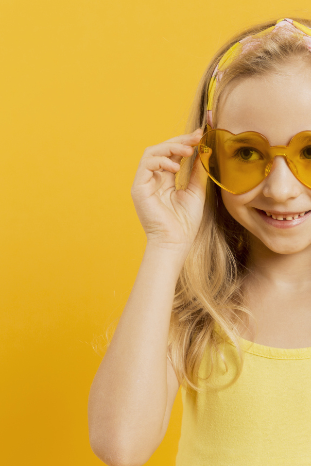 Красивая девочка блондинка в очках в форме сердца на желтом фоне