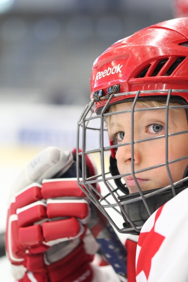 Мальчик в красном шлеме хоккеиста на поле