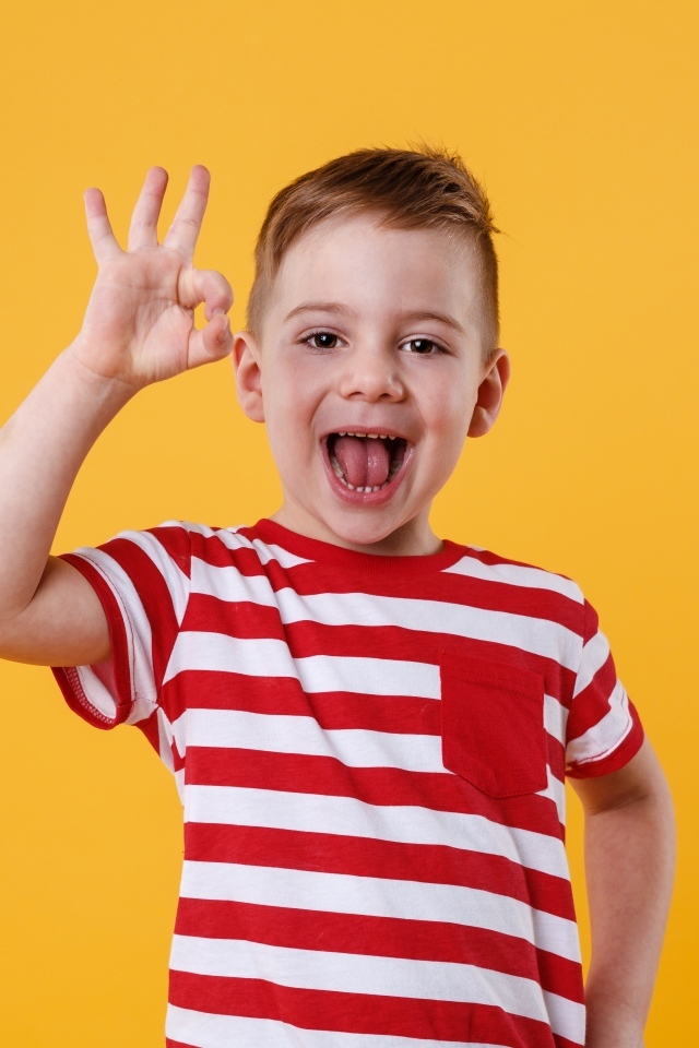 Веселый мальчик в полосатой футболке на оранжевом фоне