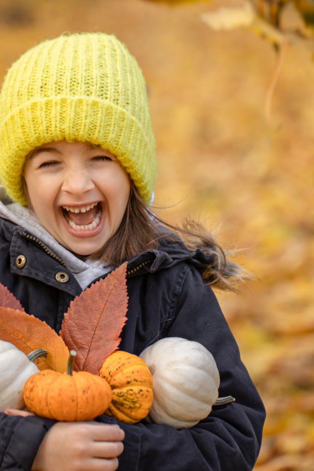 Веселая девочка с тыквами и листьями в руках осенью