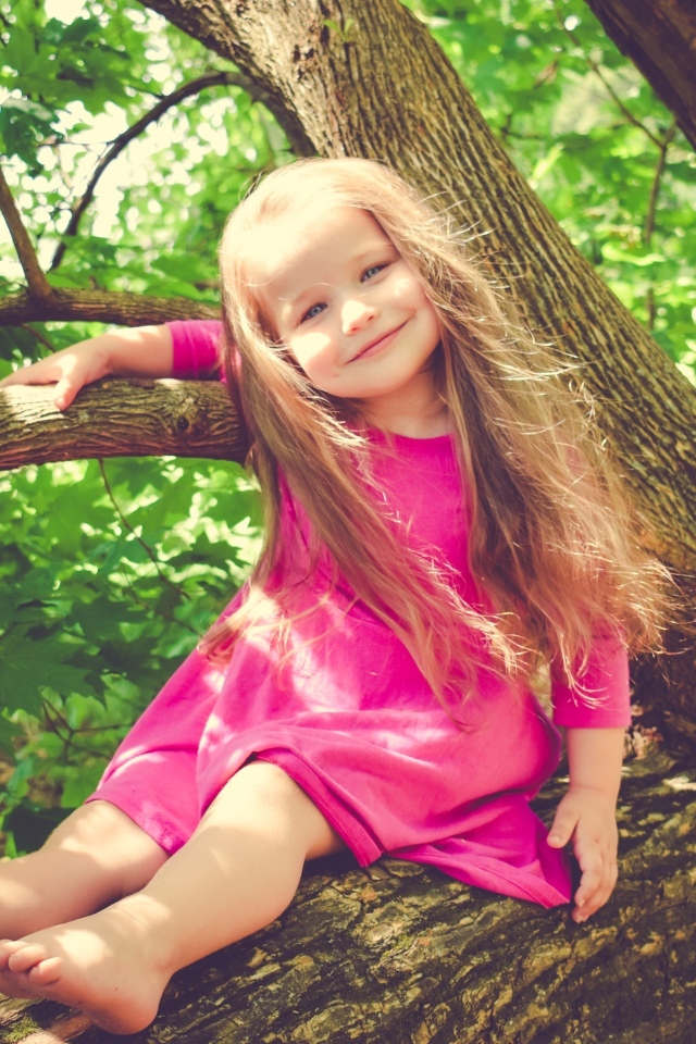 Милая девочка в розовом платье сидит на ветке дерева