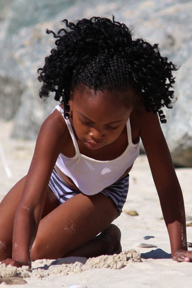 Темнокожая маленькая девочка играет на песке на пляже