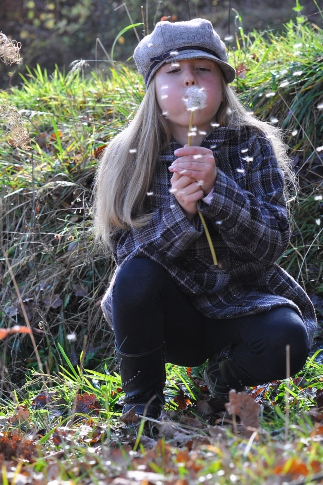 Девочка в кепке дует на одуванчик