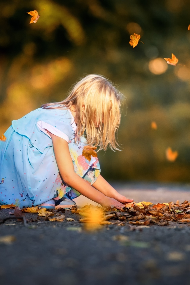 Девочка в платье играет с листьями на дороге