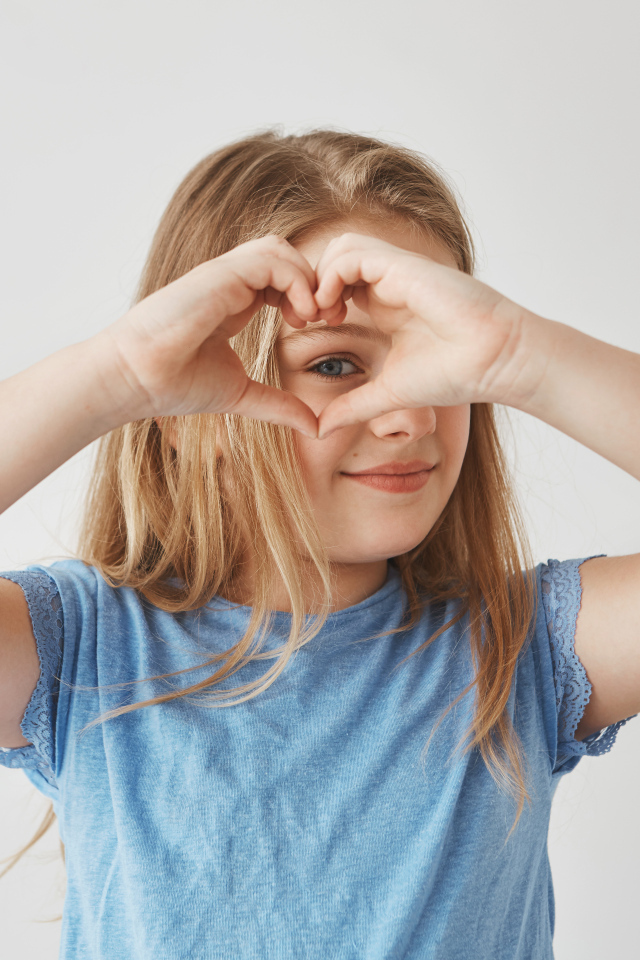 Девочка делает сердечко руками на сером фоне