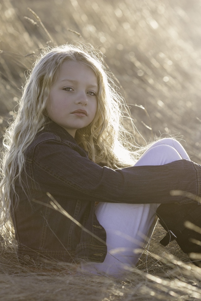 Маленькая светловолосая девочка сидит на сене