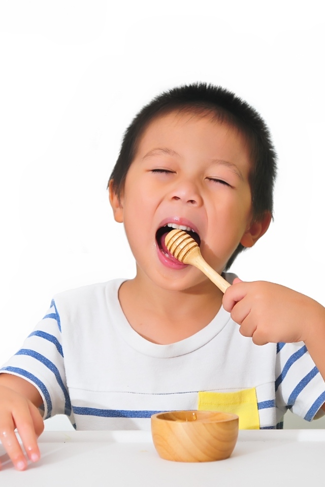 Маленький мальчик ест мед на белом фоне