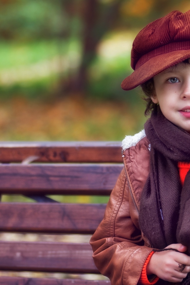 Маленький мальчик в куртке на лавке в парке осенью