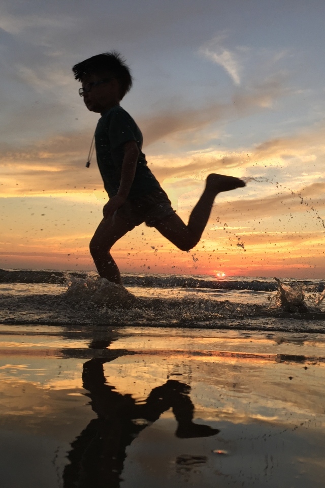 Маленький мальчик бежит по воде на закате
