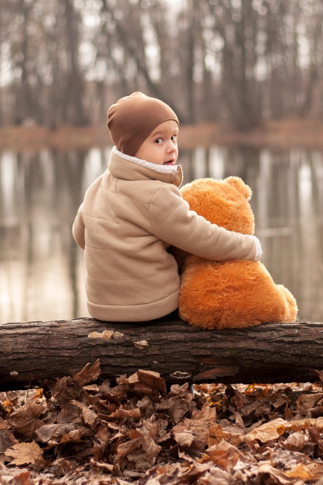 Маленький мальчик с игрушкой сидят на колоде у озера осенью