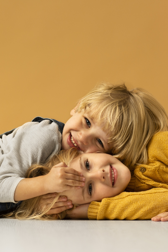 Маленькие брат и сестра лежат на полу на желтом фоне