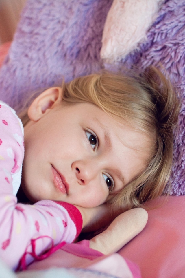 Маленькая кареглазая девочка лежит в кровати 