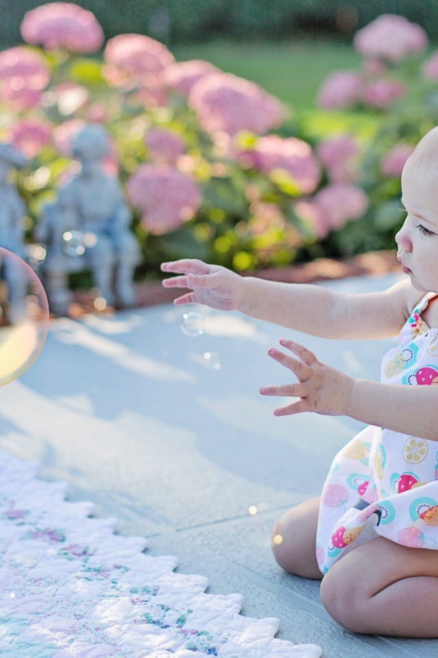 Маленькая девочка ловит мыльный пузырь