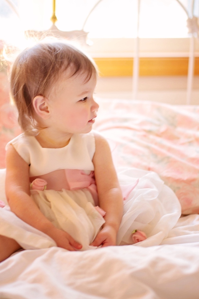 Маленькая девочка в платье сидит на кровати