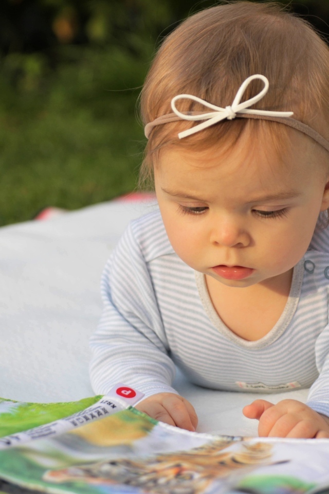 Маленькая девочка с книгой на белом покрывале