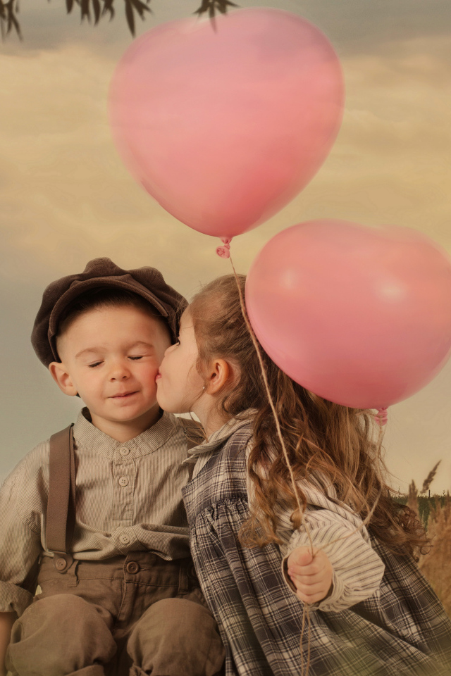 Маленькая девочка с шариками целует мальчика