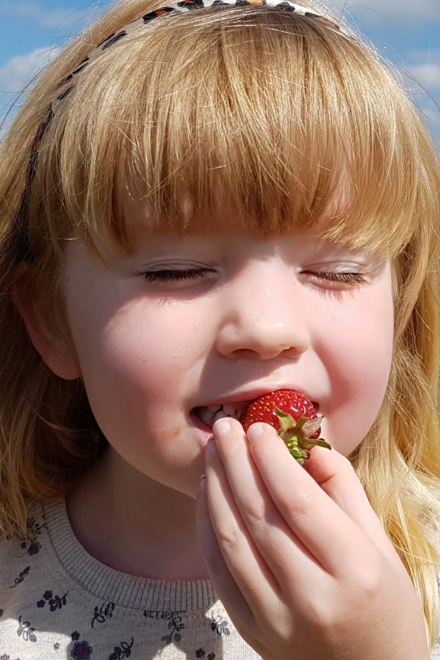 Маленькая девочка с закрытыми глазами пробует клубнику