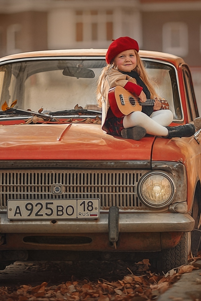Маленькая девочка с гитарой сидит на красном автомобиле осенью
