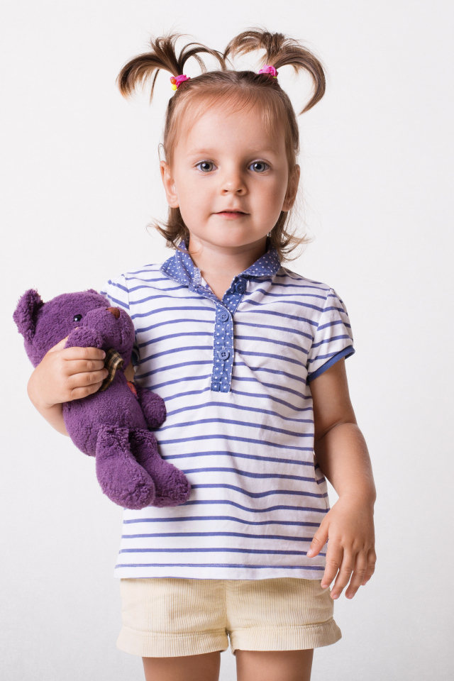 Маленькая девочка с игрушечным медведем на сером фоне