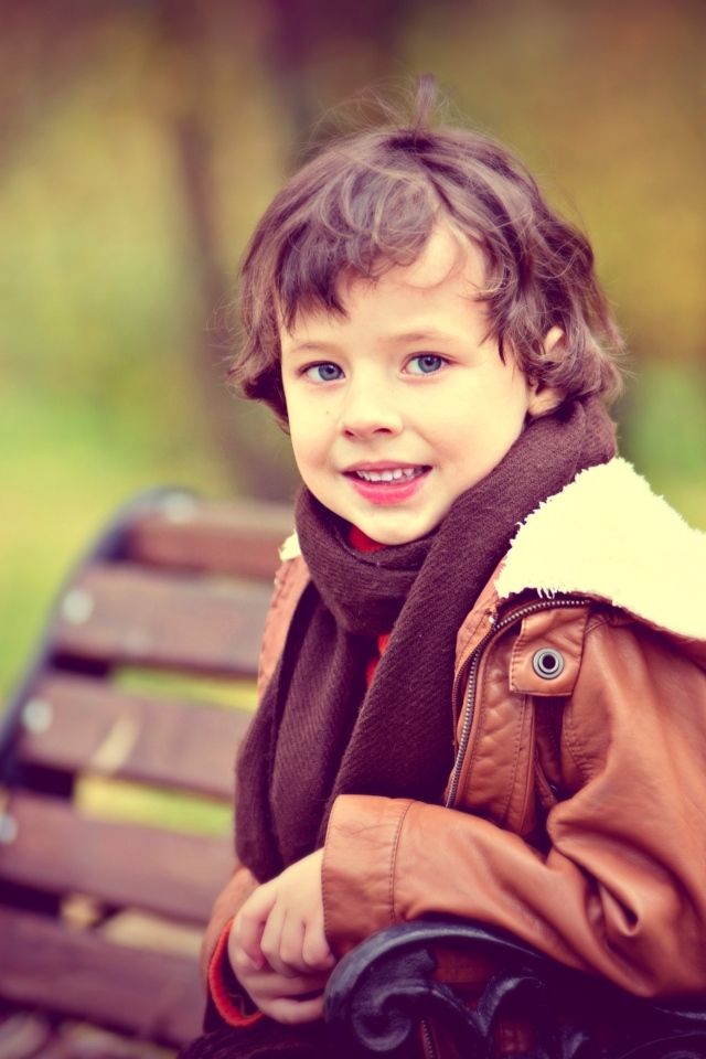 Маленький улыбающийся мальчик на лавке в парке