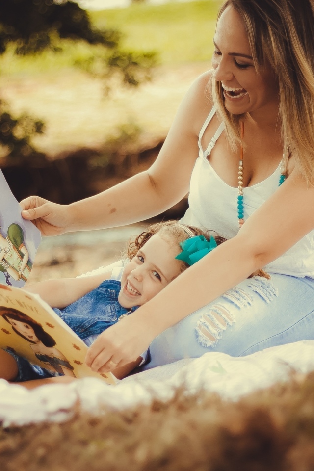 Мама читает дочери книгу на природе