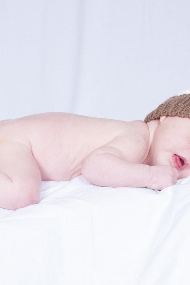 Новорожденный малыш в шапке на белой подушке