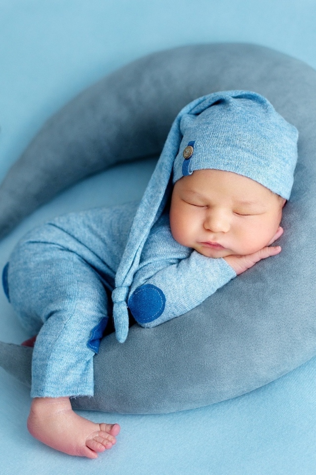 Новорожденный малыш спит на игрушечном полумесяце на голубом фоне