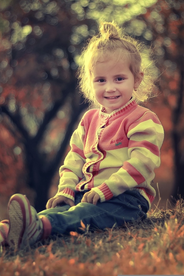 Настоящая маленькая девочка сидит на земле в лучах солнца