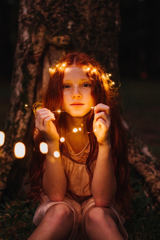 Рыжеволосая девочка с гирляндой под деревом