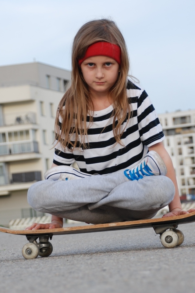 Серьезная девочка сидит на  скейтборде