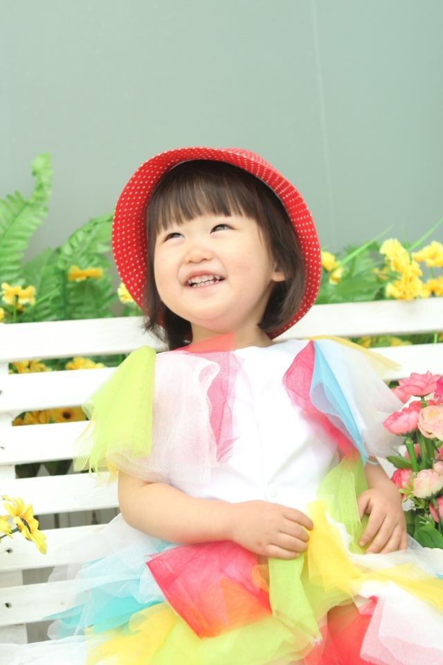 Улыбающаяся девочка азиатка сидит на лавке с цветами