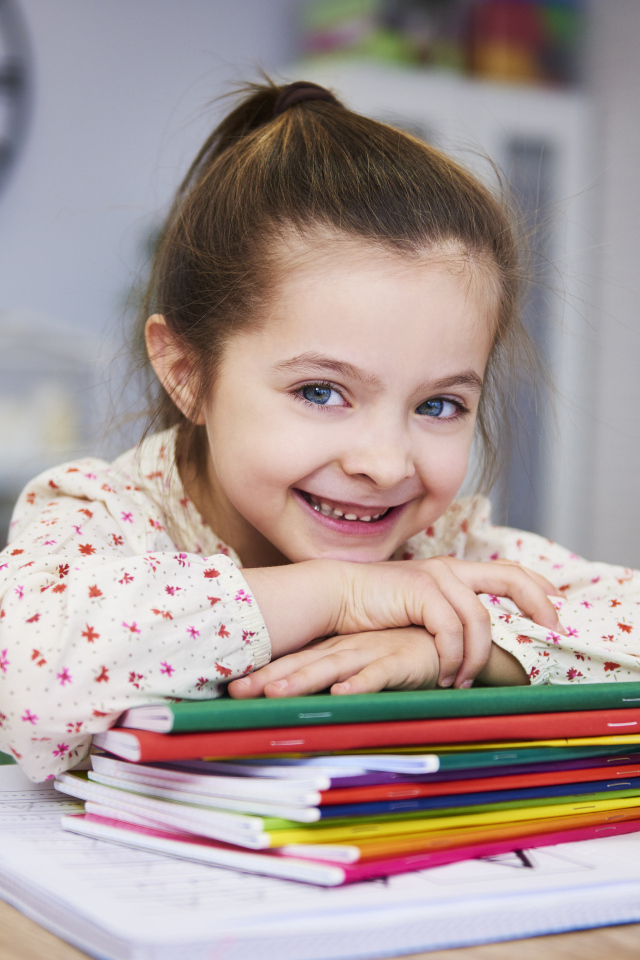 Улыбающаяся девочка ученица  с тетрадями за столом