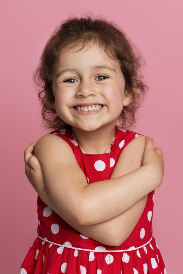 Улыбающаяся маленькая девочка в красном платье на розовом фоне